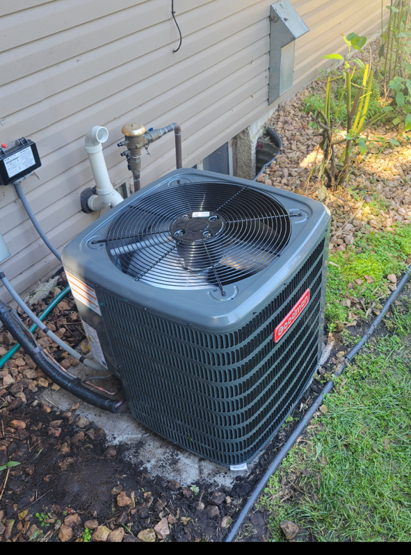 Outdoor HVAC condenser unit beside a house, with pipes and hoses along the siding.