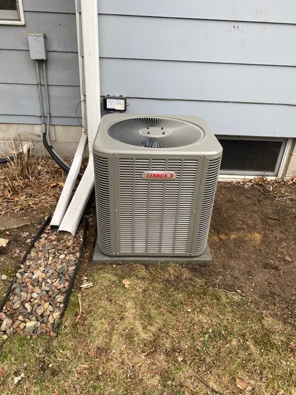 Outdoor air conditioner unit beside a house on a patchy lawn