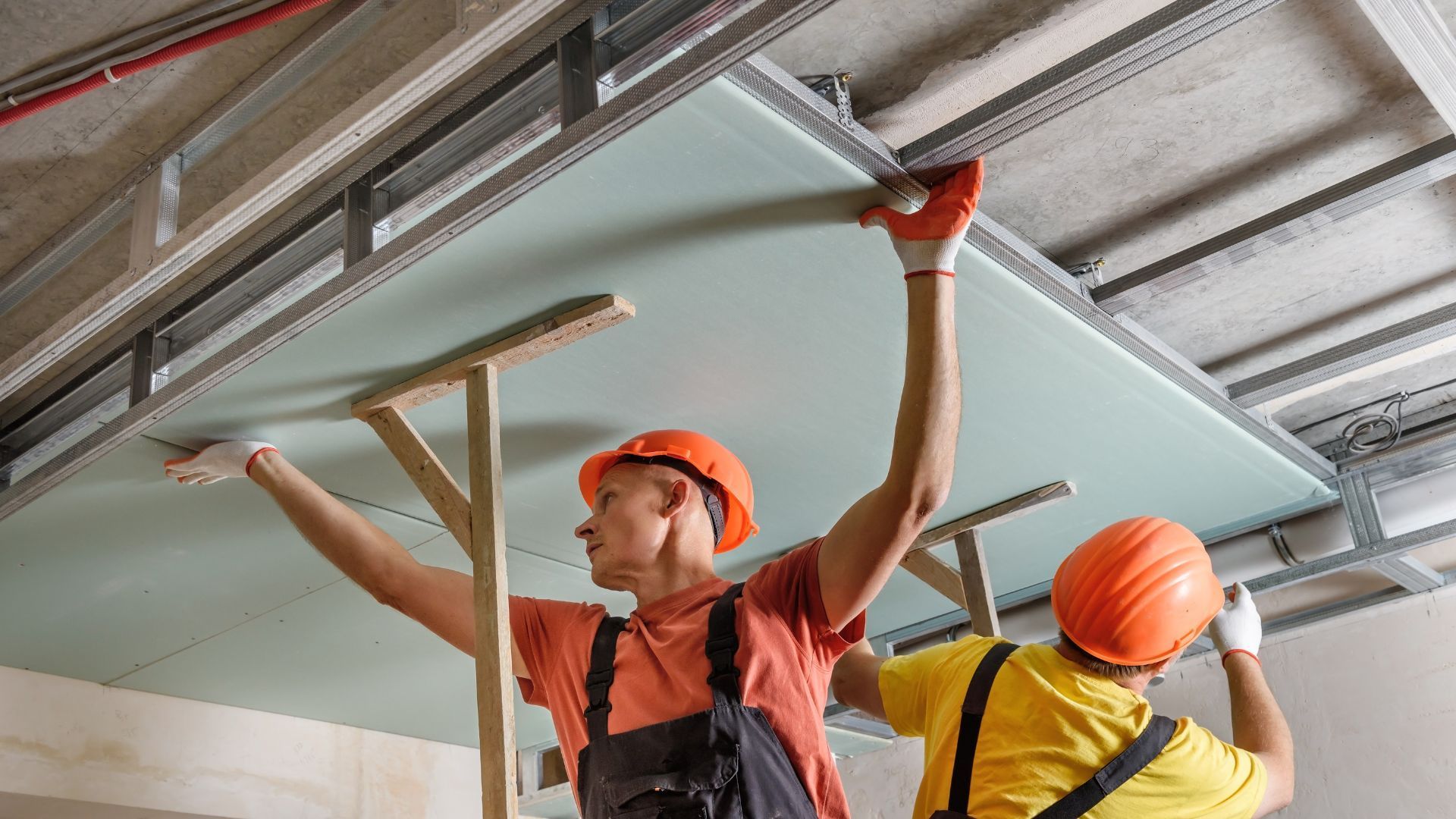 Two construction workers are working on a ceiling.