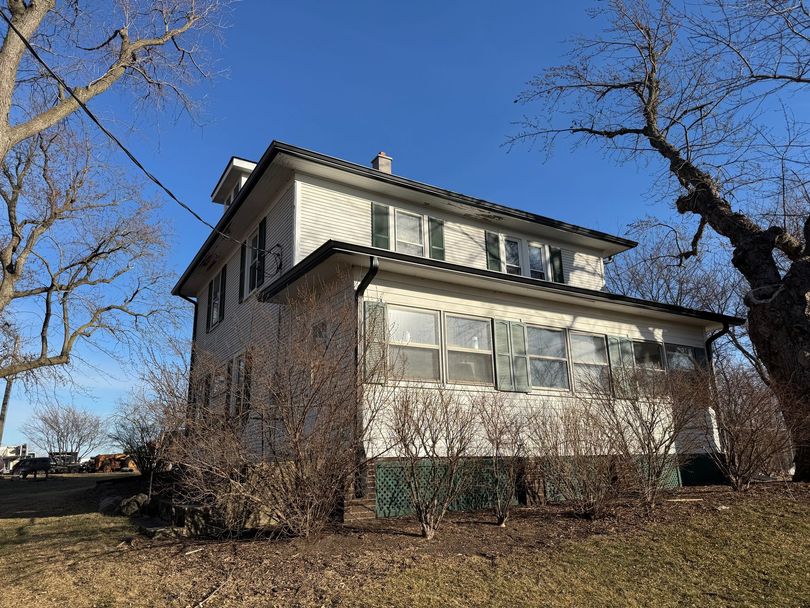Two-story white house with dark roof and screened porch, seen from a yard with leafless trees under a blue sky