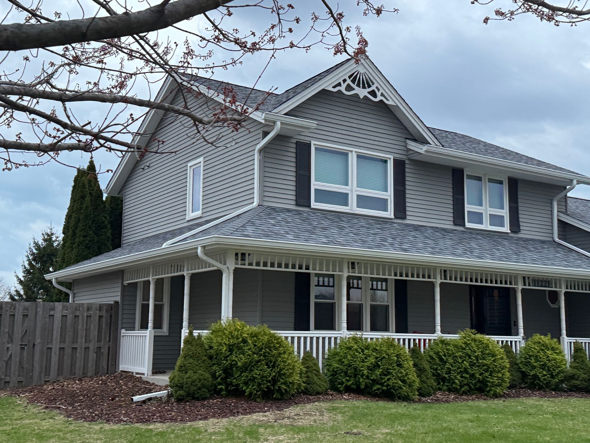 Gray two-story house with white trim and wraparound porch under cloudy skies