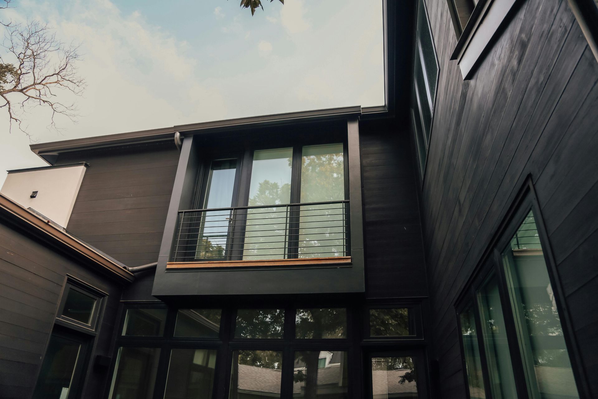Modern black house exterior with large windows and a balcony between two buildings