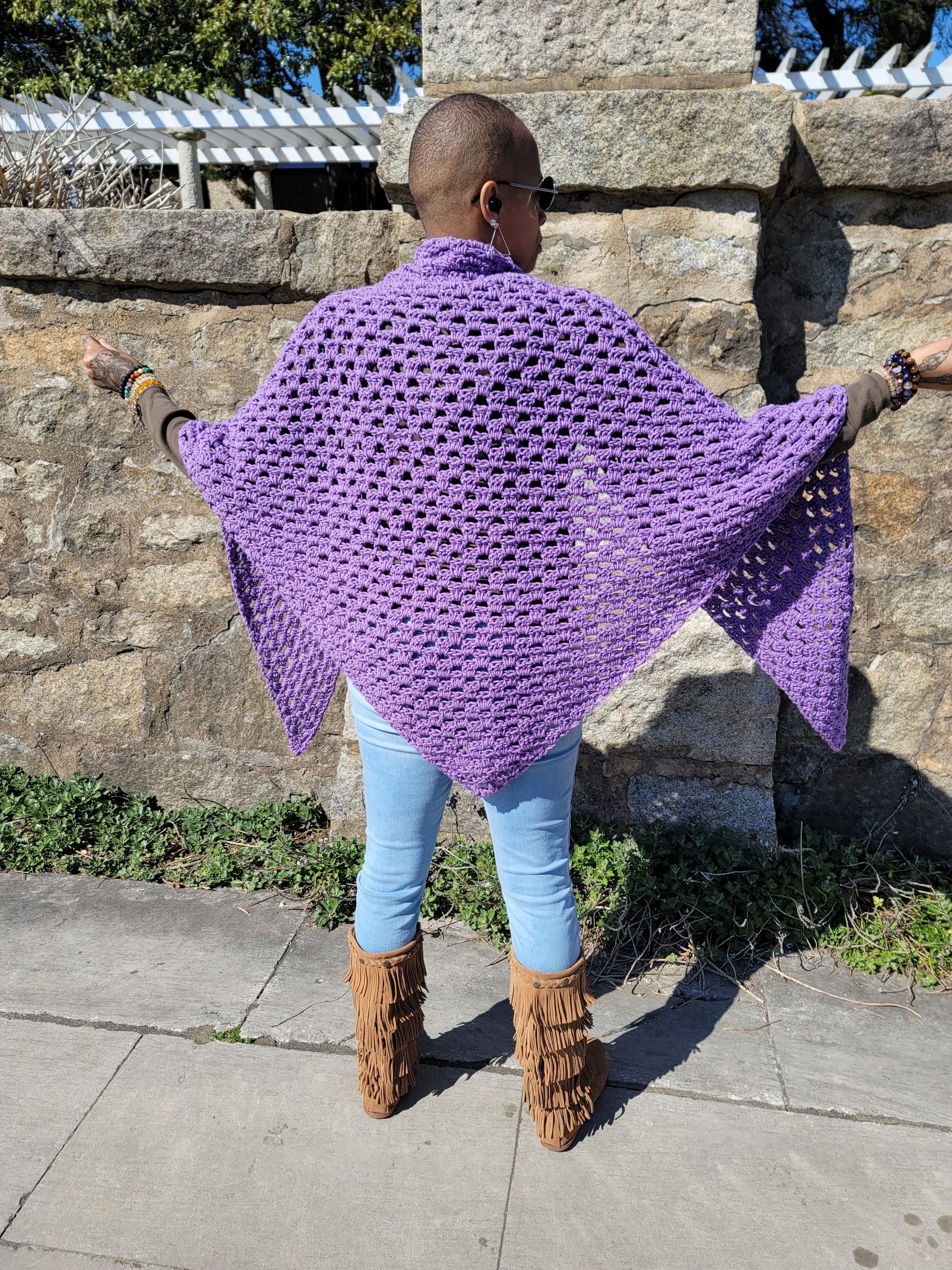 A woman wearing a purple shawl and boots is standing on a sidewalk.