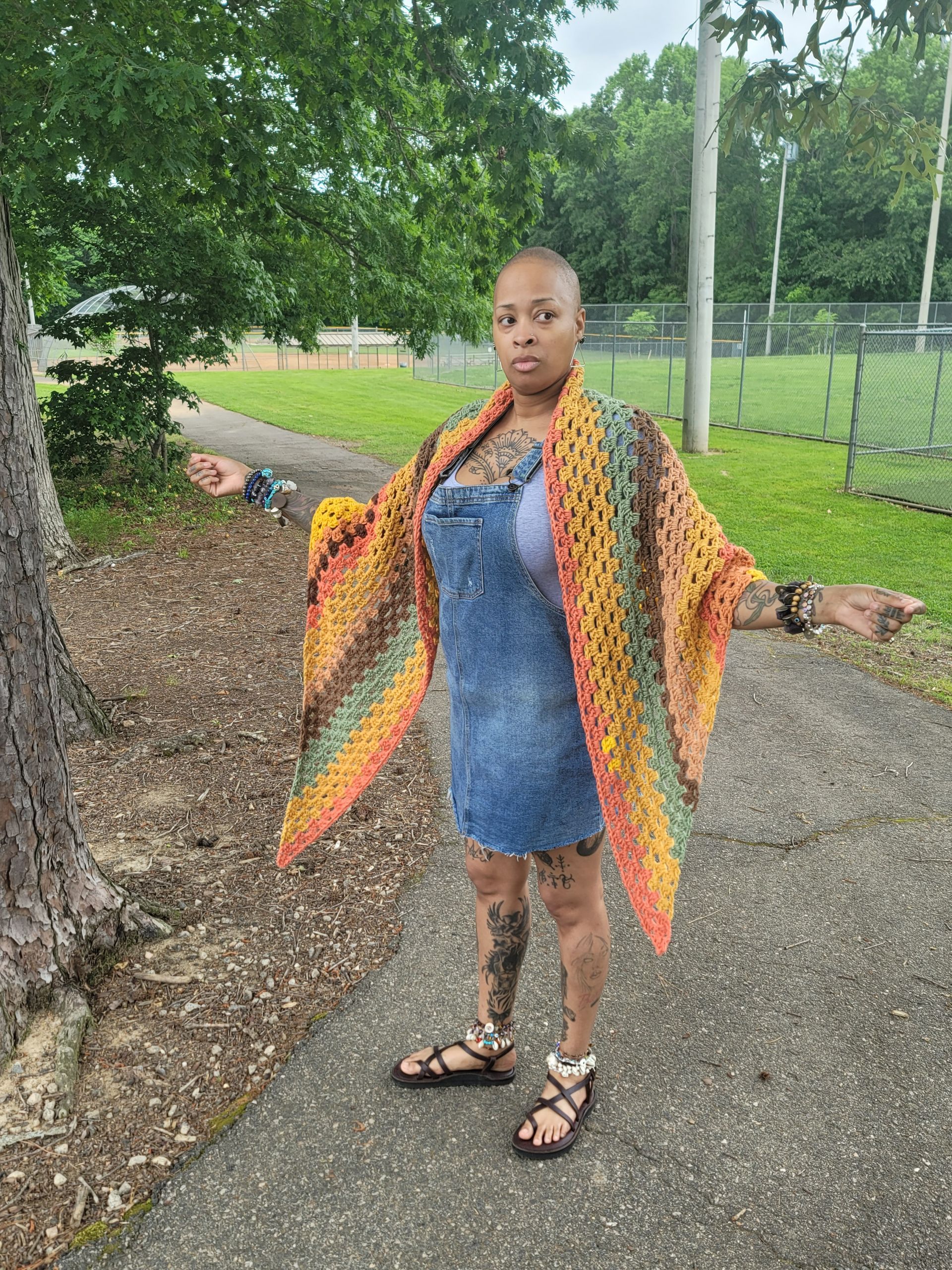 A woman is standing on a sidewalk wearing a crocheted shawl.