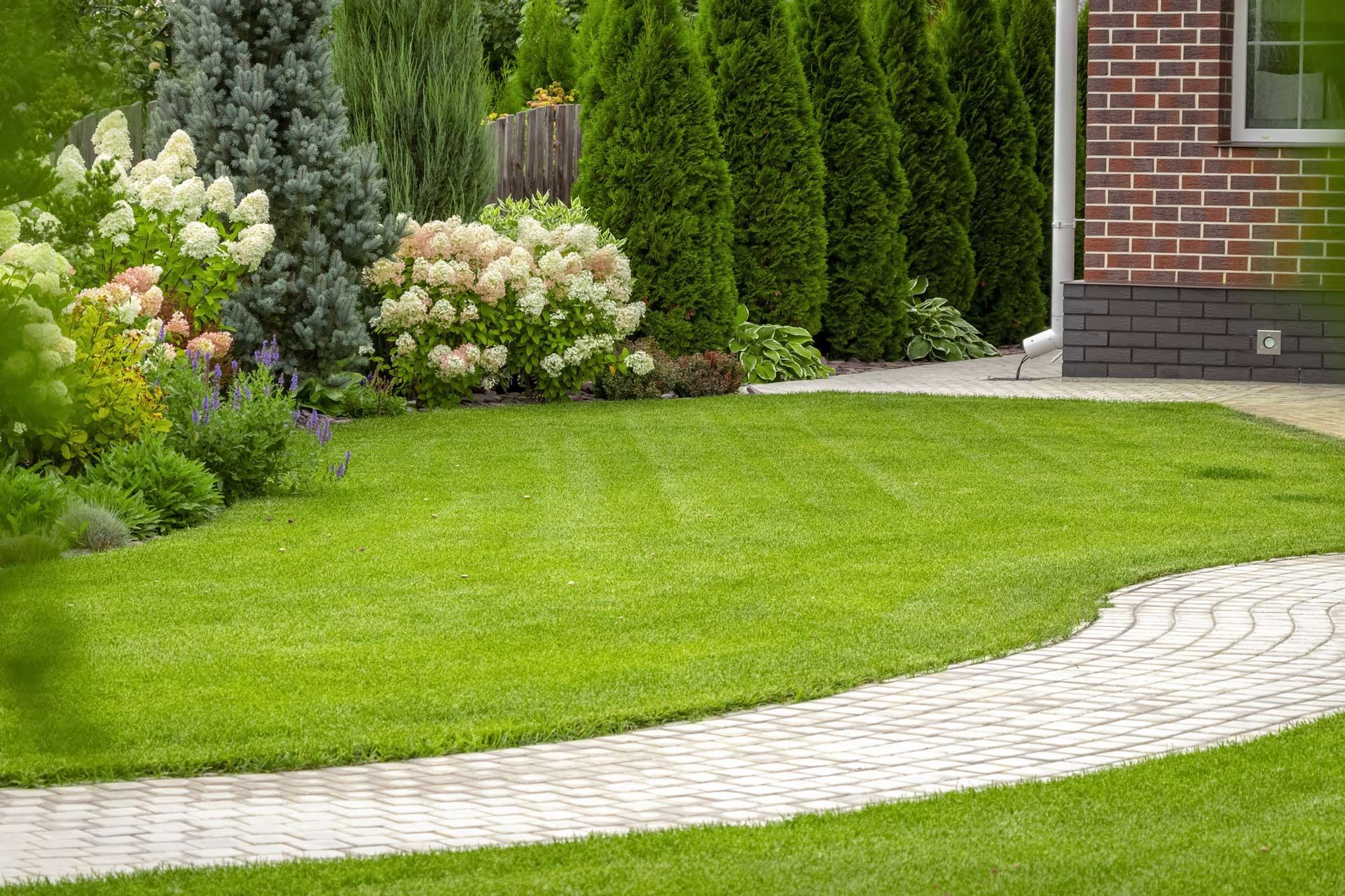 A brick walkway leading to a lush green lawn in front of a brick house