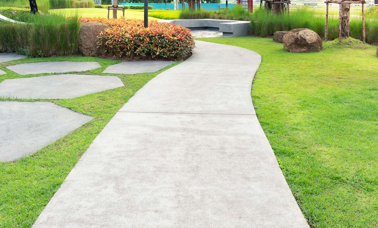 A concrete walkway in a park surrounded by grass and rocks