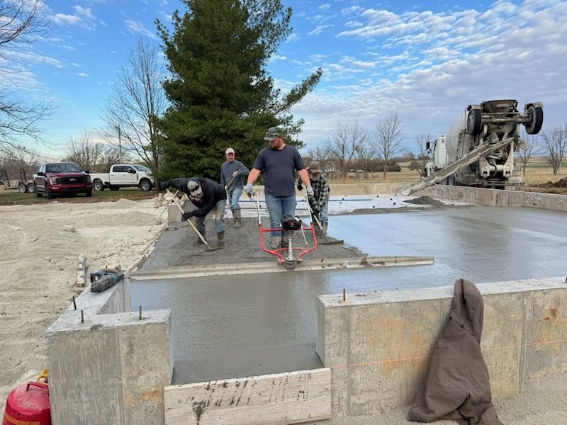 Workers smoothing wet concrete on a foundation slab beside a concrete pump truck outdoors.