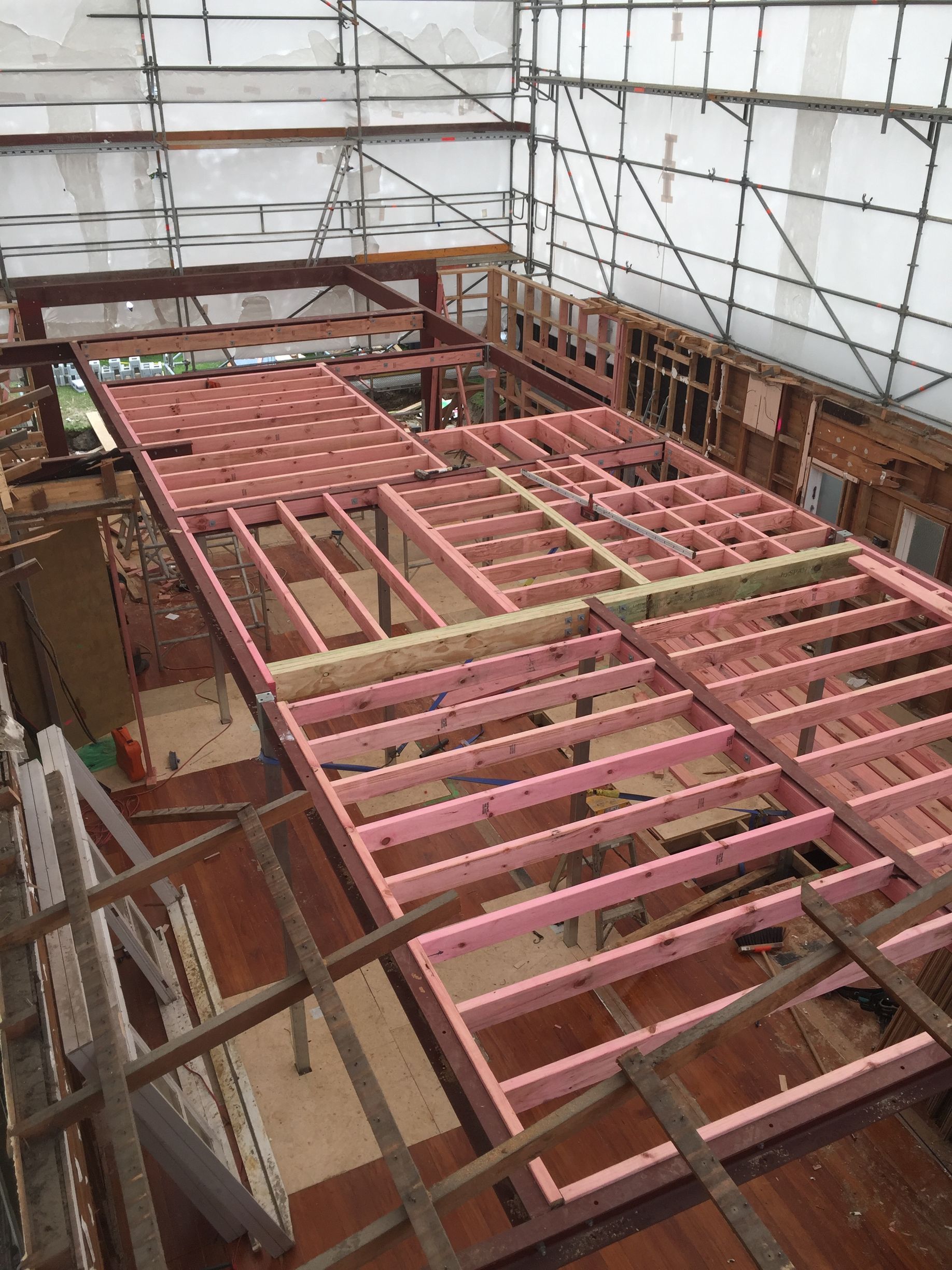Scaffolding around a building with a pink wooden roof frame under construction