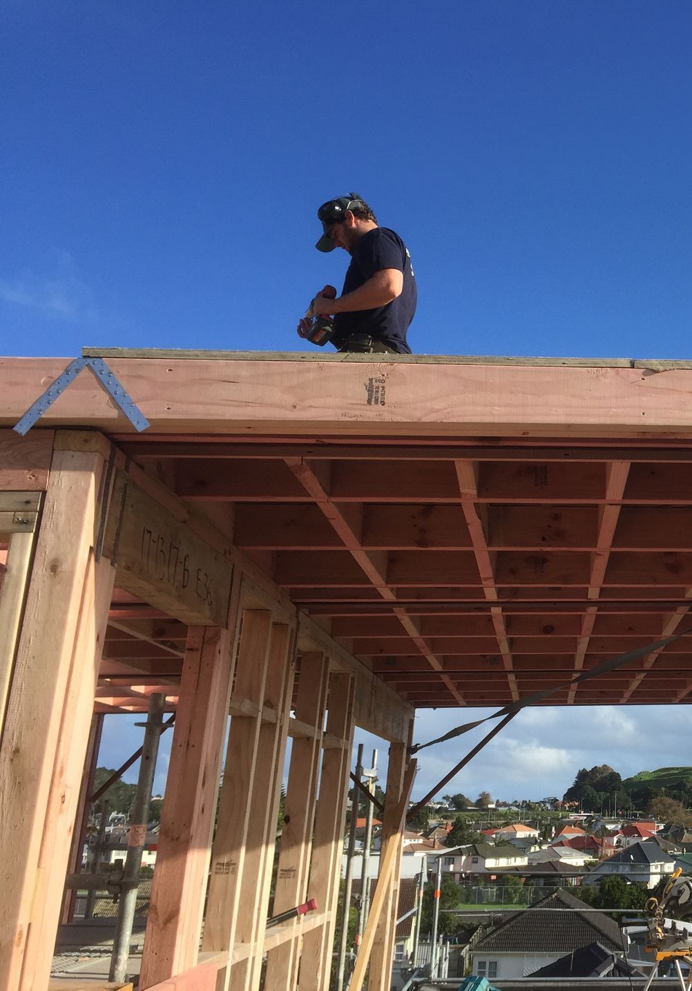 Worker crouched on a rooftop frame under a clear blue sky.
