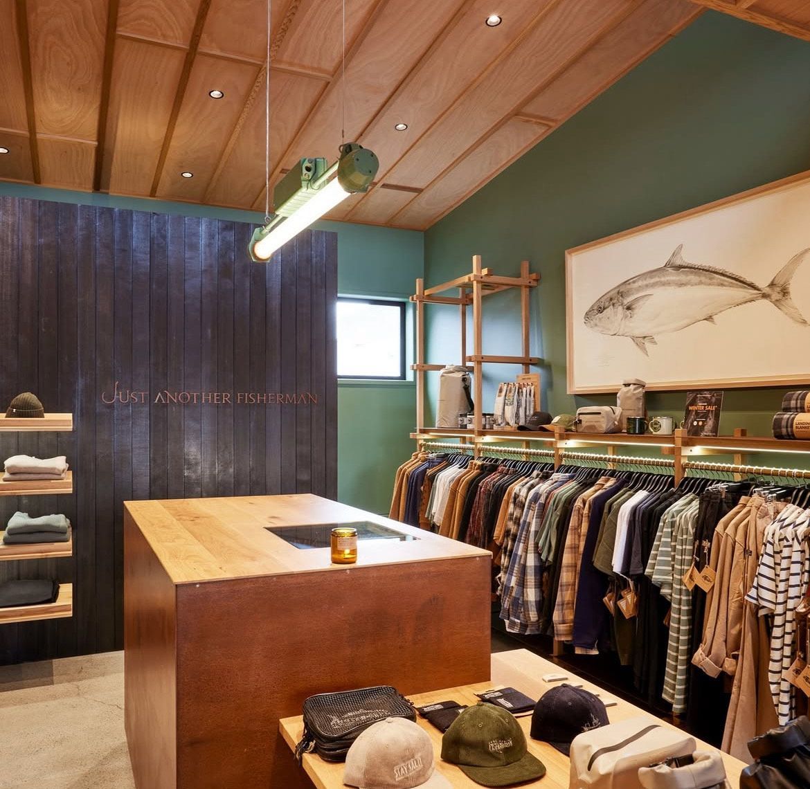 Boutique clothing store with wooden table, hanging racks, hats, and a curtained fitting area