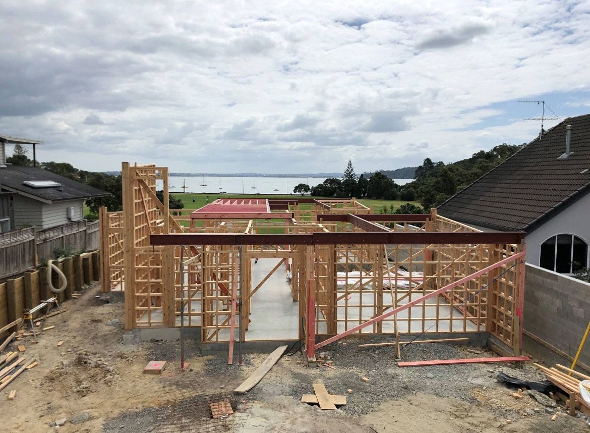 Partially built wooden house frame on a residential lot under a cloudy sky