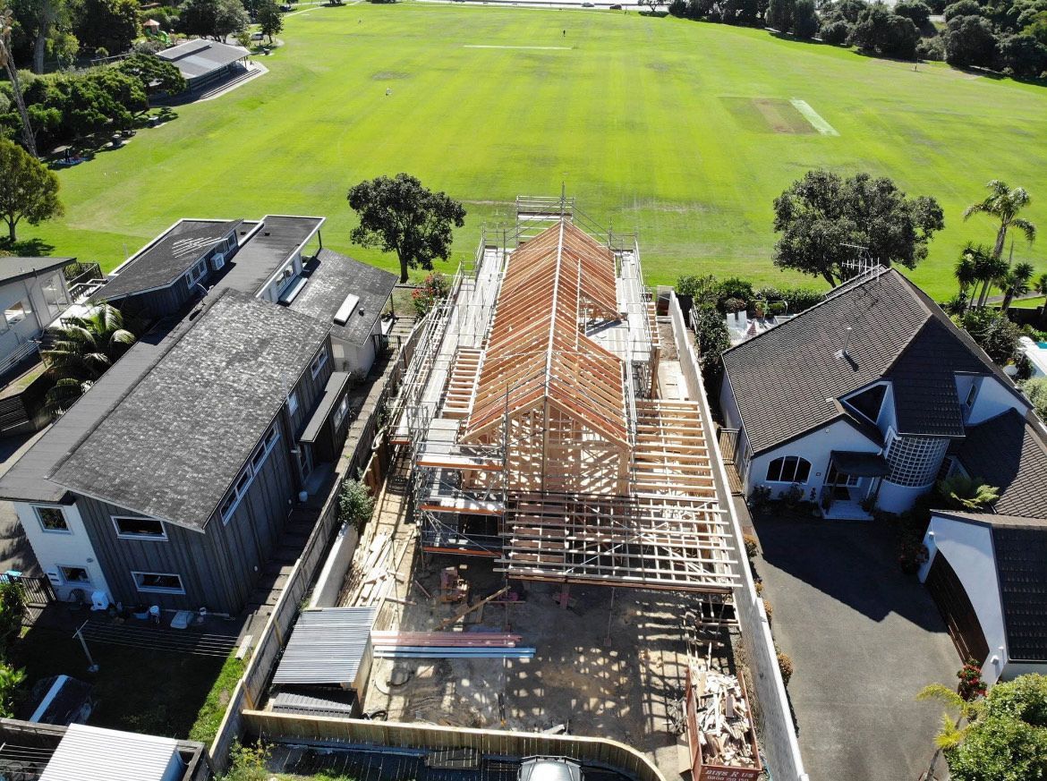 Aerial view of a house roof under construction beside green fields and neighboring homes