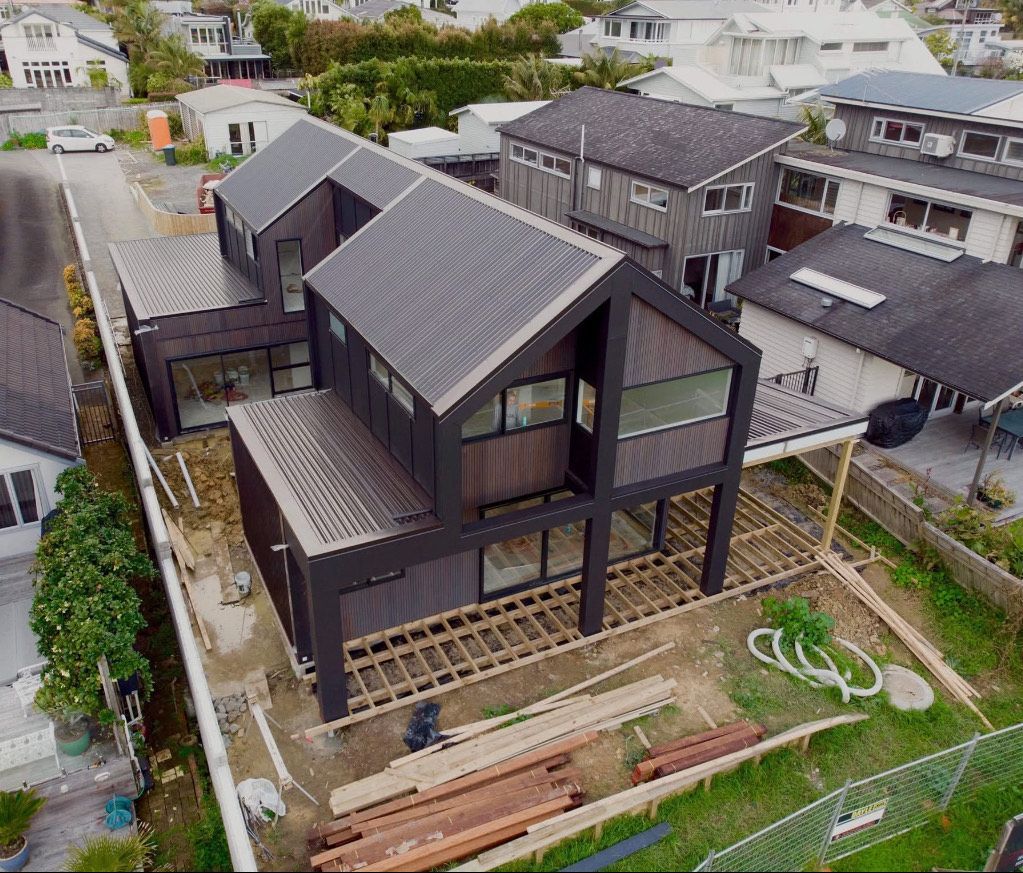 Aerial view of a modern black house under construction with exposed framing and stacked building materials in a neighborhood