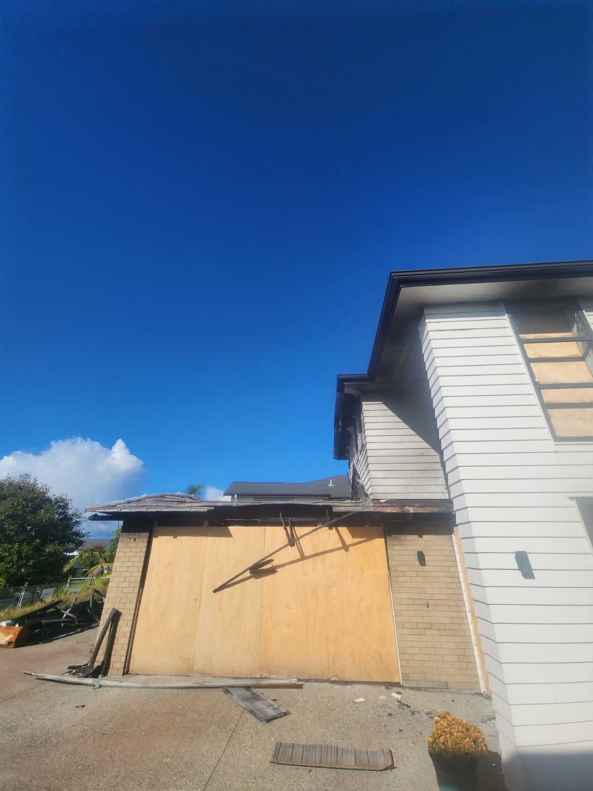 Damaged wooden garage wall beside a white house under a clear blue sky