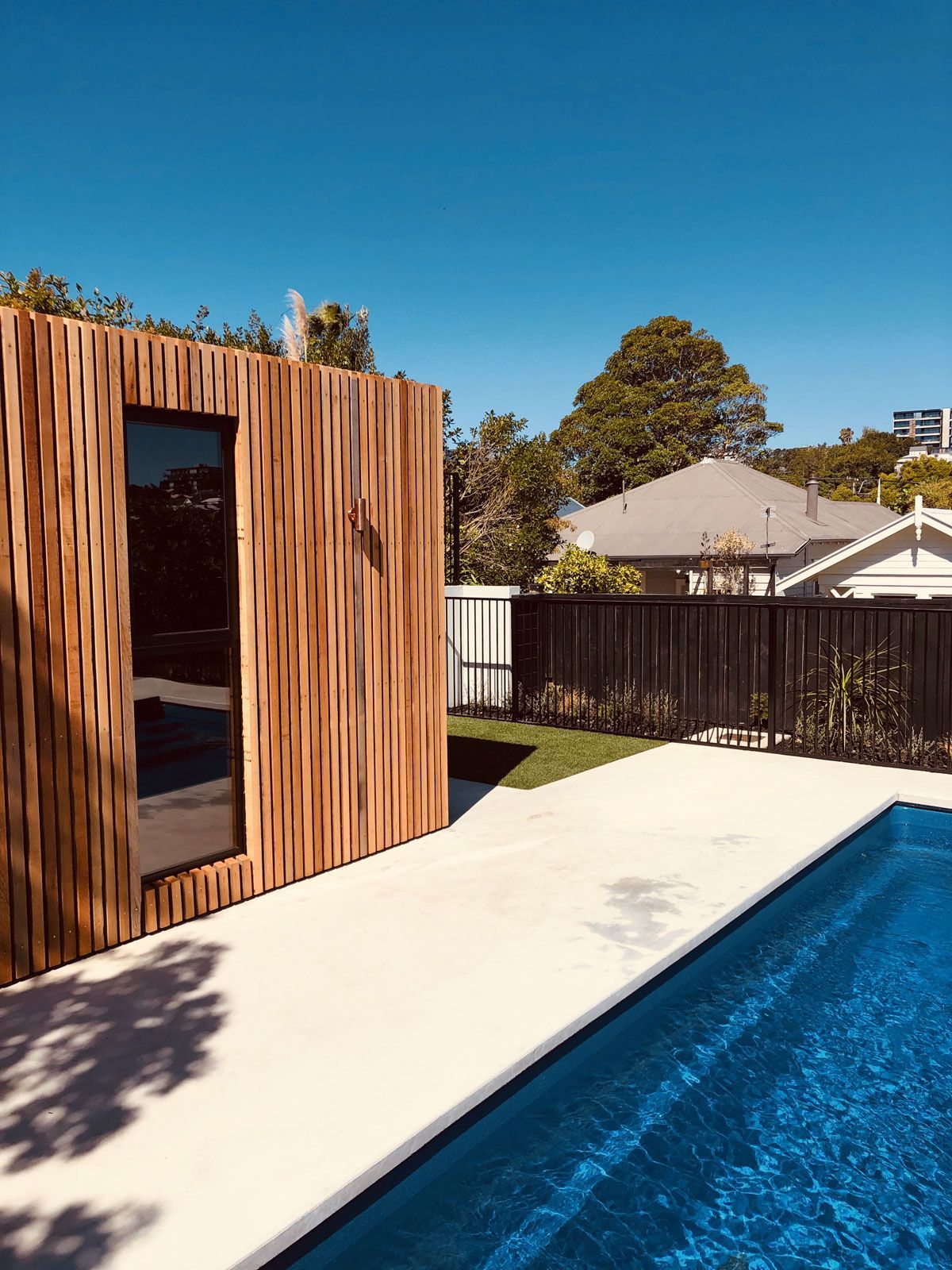 Backyard pool beside a modern wood-paneled structure under a clear blue sky