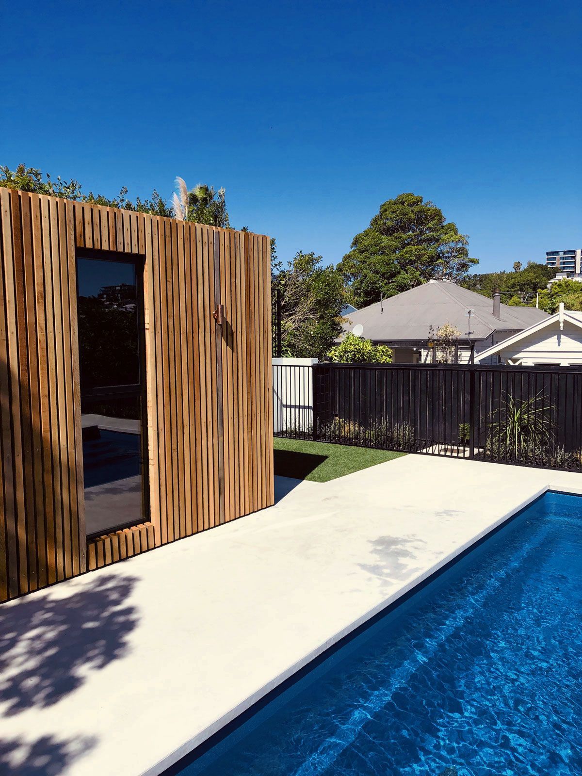 Modern poolside deck with a wooden sauna, blue water, and a clear sky