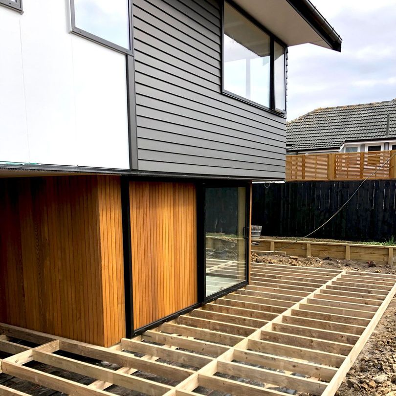 House exterior with exposed wooden deck framing and sliding glass doors under gray siding
