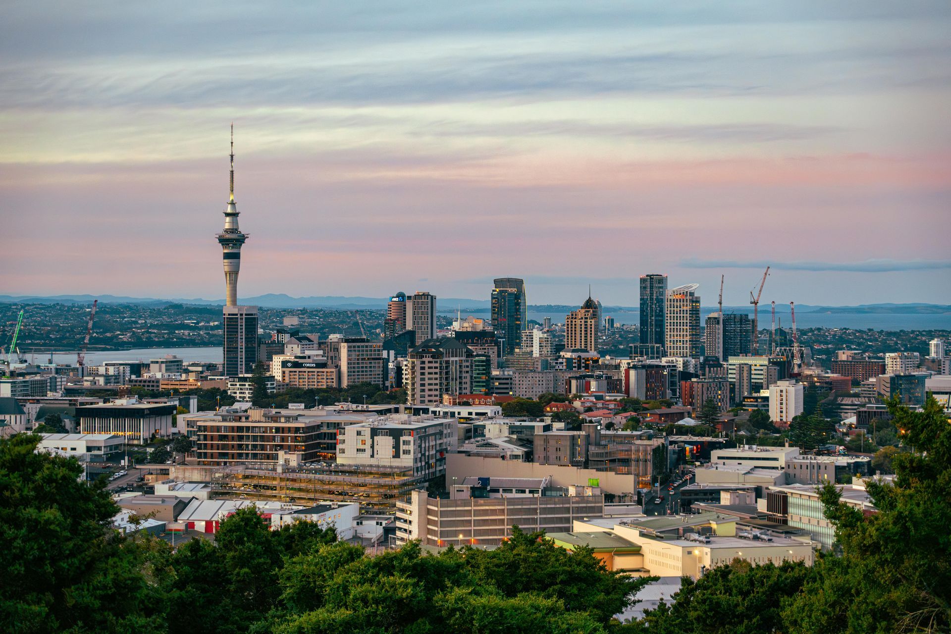 City skyline at dusk with a tall tower, modern buildings, and a pastel sunset sky
