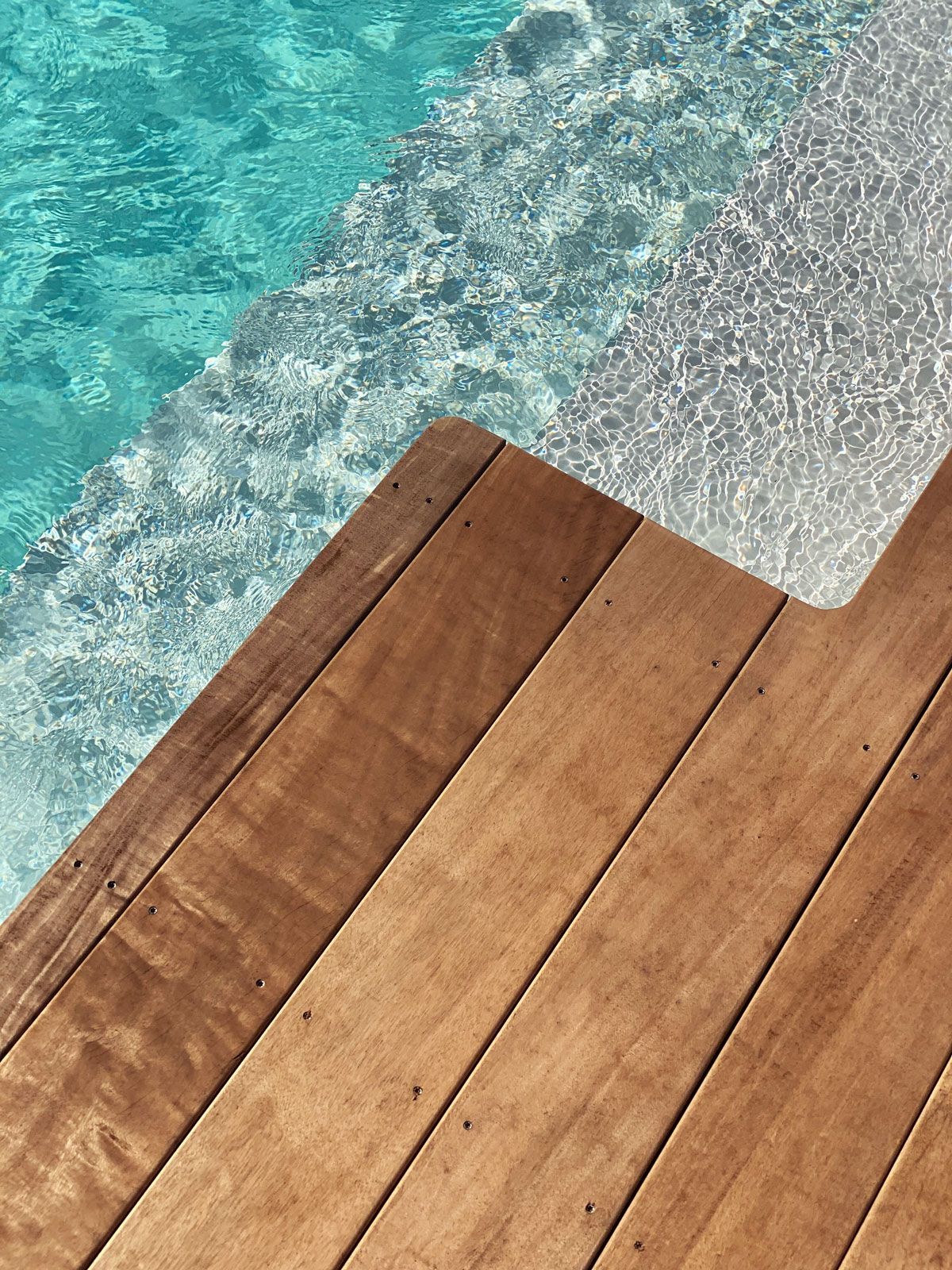 Wooden deck beside turquoise pool water with a shimmering edge
