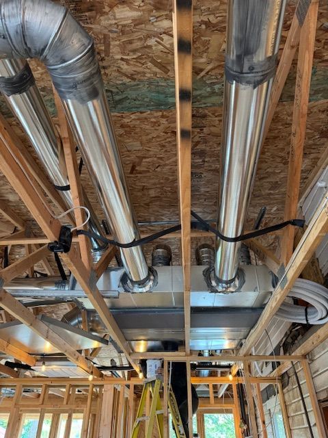 Exposed HVAC ductwork and pipes in an unfinished house ceiling with exposed wooden framing.