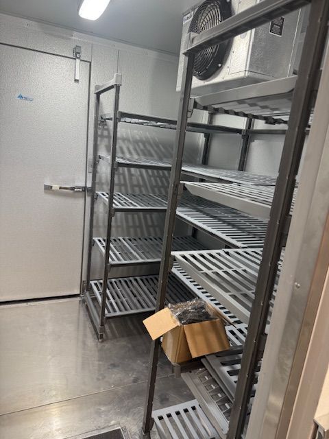 Walk-in storage room with metal shelving, a closed door, and a cardboard box on the floor