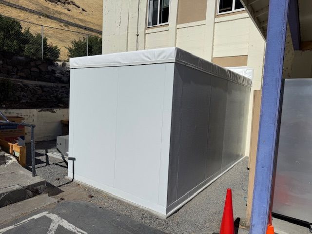 White temporary shed beside a building with a red cone in an outdoor lot