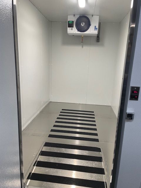 Empty elevator interior with a black-striped floor and a wall-mounted fan unit above.
