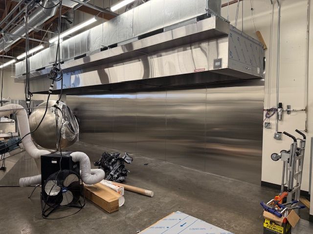 Industrial ventilation system with large metal hood, ducting, and equipment in a factory-like room