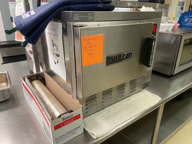 Stainless steel Vulcan countertop oven on a kitchen prep table with a roll of foil and towels on top