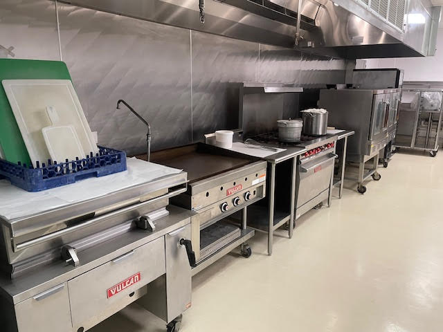 Commercial kitchen prep line with stainless steel counters, pots, and dish racks along a wall