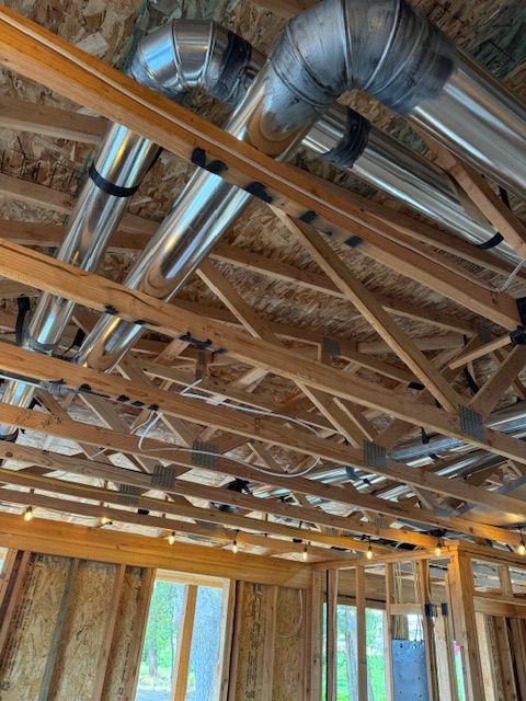 Exposed wooden roof framing with shiny metal HVAC ducts inside a building under construction