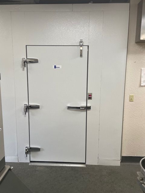 White walk-in cooler door with metal handles in a commercial kitchen area.