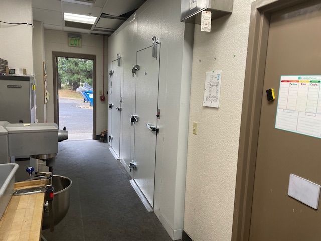 Narrow utility hallway with white doors, tan walls, and an open doorway to outside light.