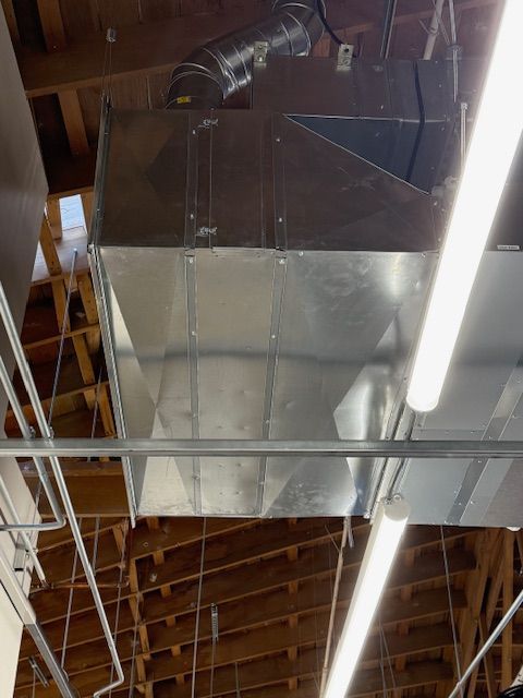 Metal HVAC ducting and fluorescent lights on a wooden-ceilinged industrial interior.