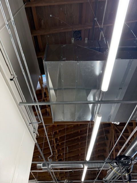 Industrial ceiling with exposed beams, ducts, and bright fluorescent lights in a warehouse-like interior