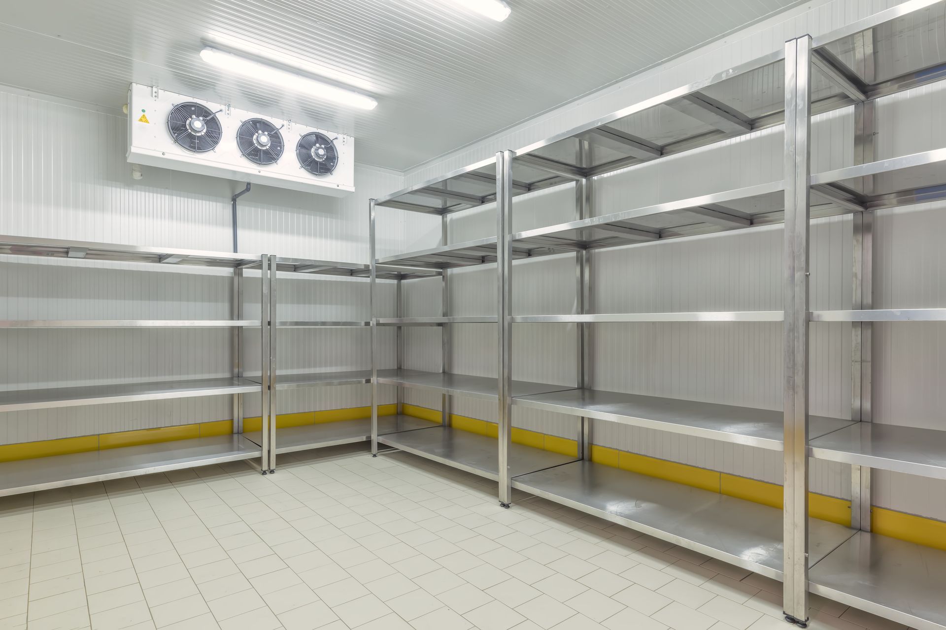 Empty, industrial walk-in freezer with metal shelves, air conditioning unit, and tiled floor.