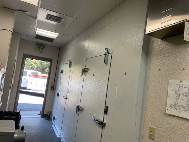 Long hallway with ceiling lights, wall-mounted shelves, and a glass exit door at the end.
