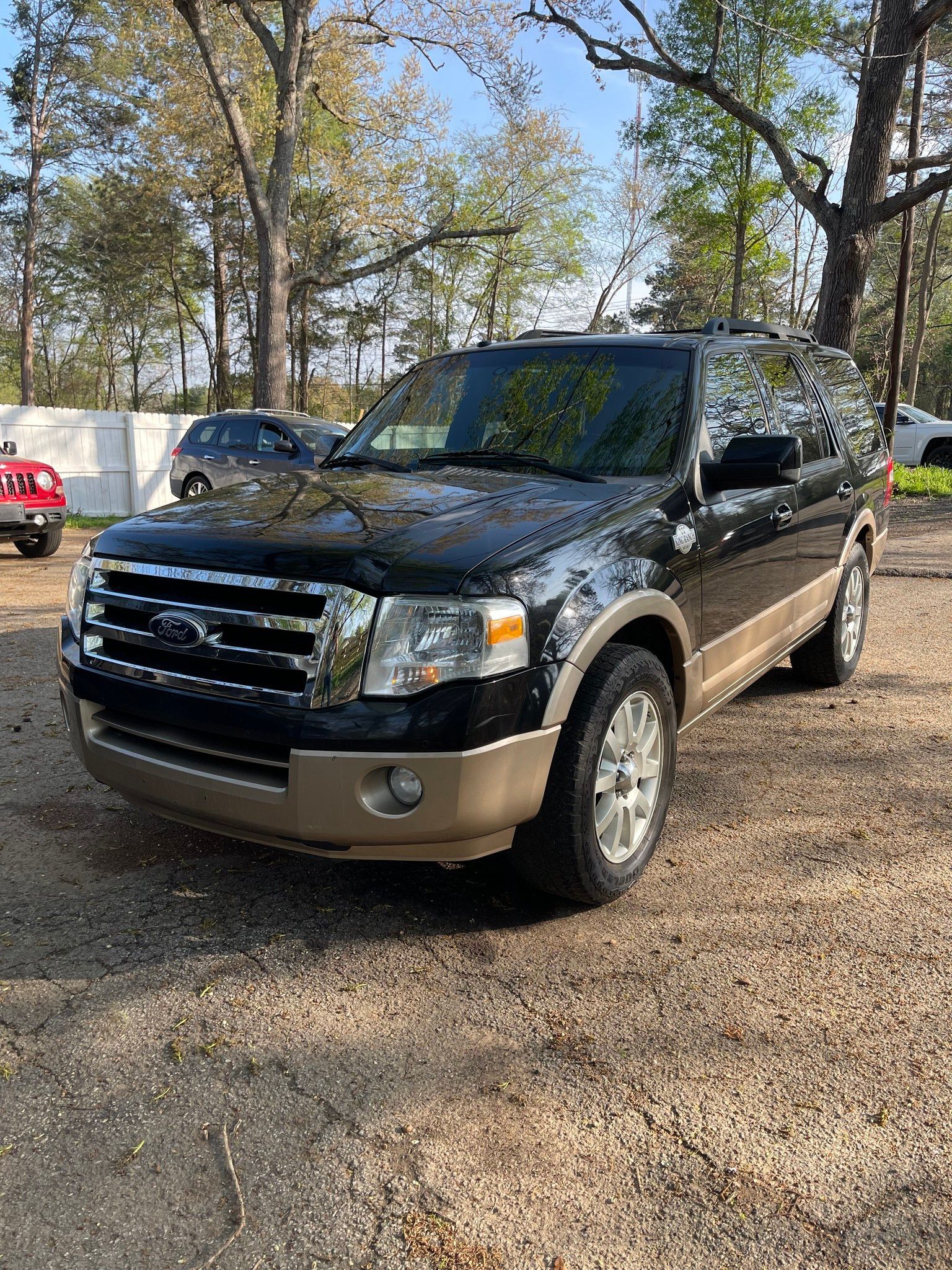 Black Ford SUV parked on a gravel lot with trees in the background.