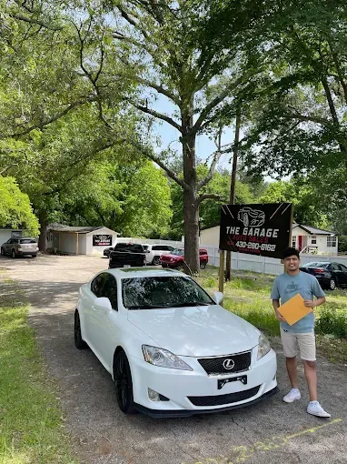 White Honda parked outdoors beside a man holding a folder under a tree and sign.