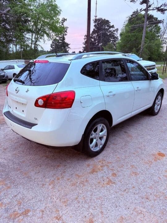 White hatchback parked on a gravel lot at dusk, with trees and other cars in the background.