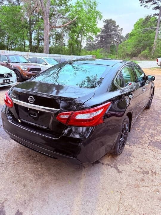 Black Nissan sedan parked outdoors on a driveway with trees and other cars in the background