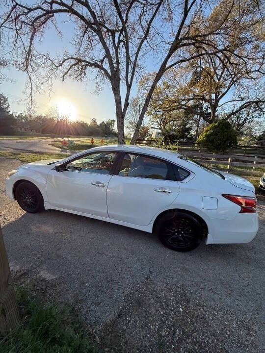 White sedan parked on a rural roadside at sunset, with bare trees and a wooden fence in the background.