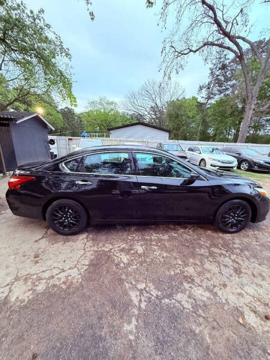 Black sedan parked in a driveway beside several cars, with trees and houses in the background