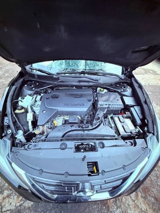 Car engine bay with hood open, showing the battery, engine cover, and front grille.