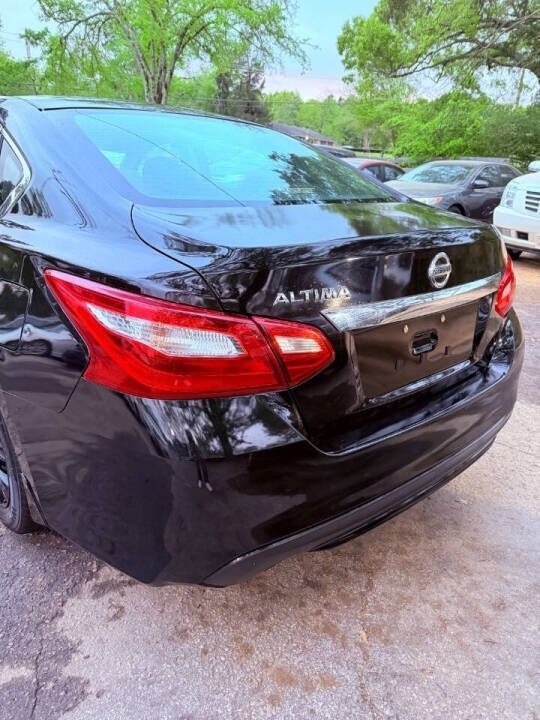 Black Nissan Altima sedan parked outdoors, rear view with red taillights and trees in the background.