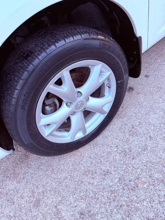 Close-up of a car’s silver wheel and black tire on a light concrete surface.