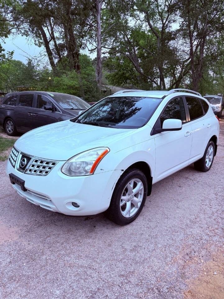 White Nissan SUV parked on a gravel lot with trees in the background.