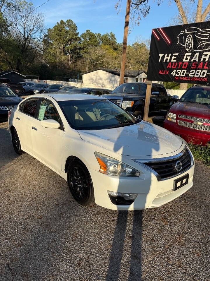 White sedan parked in a car lot beside a dealership sign, with other cars and trees in the background