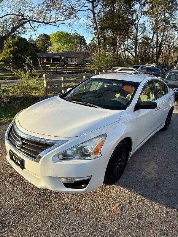 White sedan parked on a gravel driveway beside a fence and trees in late-afternoon light