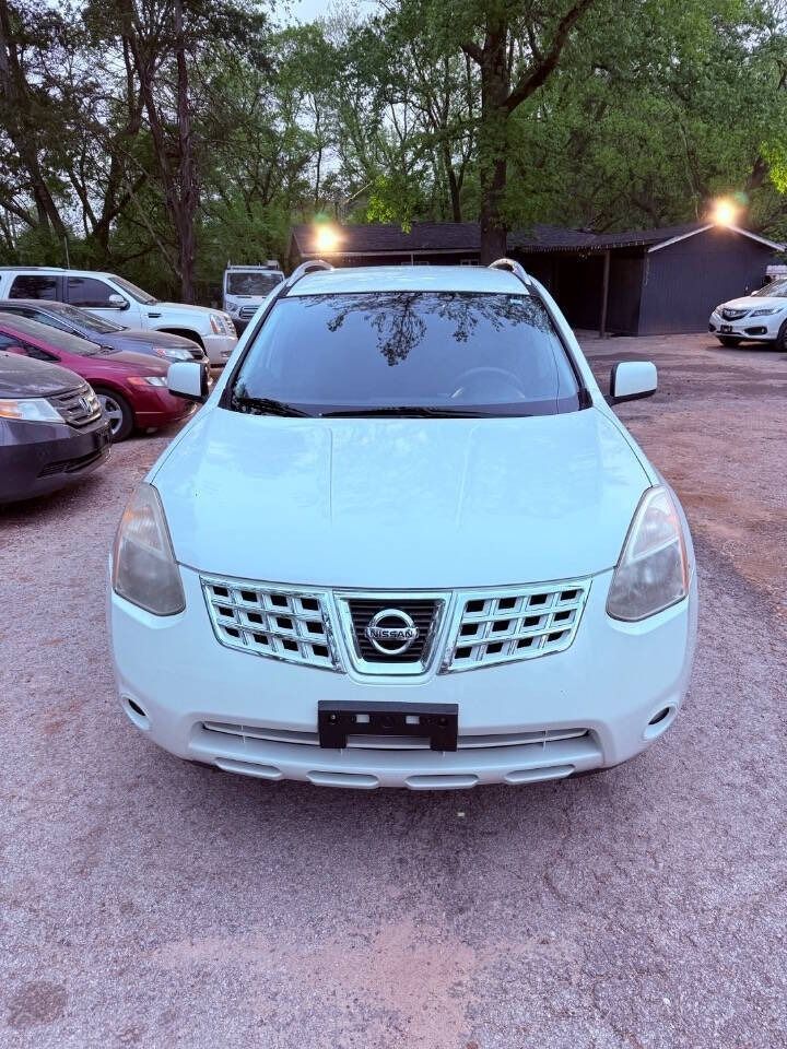 White Nissan SUV parked in a gravel lot at dusk, with cars and trees in the background